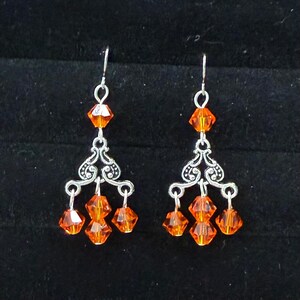 May include: A pair of chandelier earrings with orange faceted beads and ornate silver-tone metalwork. The earrings have a dangling design with multiple beads and a decorative filigree pattern.