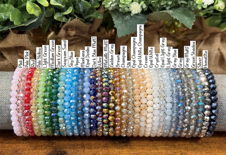 Peut inclure: Une collection de bracelets en perles de cristal &agrave; facettes dispos&eacute;s en rang&eacute;e, chacun &eacute;tiquet&eacute; avec des noms de couleurs comme Pink, Red, Aqua, Wine, Champagne et Hematite. Les bracelets pr&eacute;sentent un spectre de couleurs vari&eacute;es.