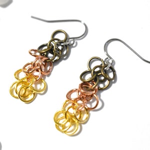 May include: A pair of gold, copper, and bronze chain earrings with silver hooks. The earrings are made of multiple small rings that are linked together in a cascading pattern.