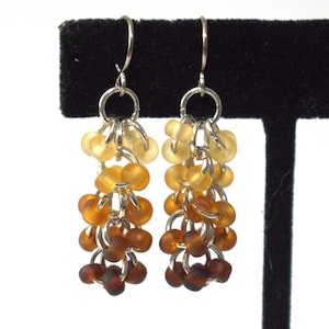 May include: A pair of dangle earrings with a gradient of amber colored glass beads. The beads are strung on silver chain and the earrings have silver hooks.