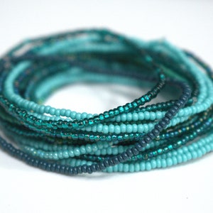 May include: A stack of teal and turquoise beaded bracelets. The bracelets are made of small, round beads and are arranged in a circular pattern.