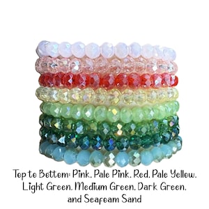 Peut inclure: Une pile de huit bracelets de perles en cristal &agrave; facettes dans un spectre de couleurs. Les couleurs de haut en bas sont rose, rose p&acirc;le, rouge, jaune p&acirc;le, vert clair, vert moyen, vert fonc&eacute; et sable &eacute;cume de mer. Chaque bracelet a des perles.