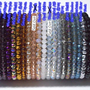 May include: A collection of faceted crystal bead bracelets arranged in a row, featuring various colors including violet, amethyst, metallic purple, gold, champagne, amber, white, gray, green, and black, with text labels identifying each color variant.