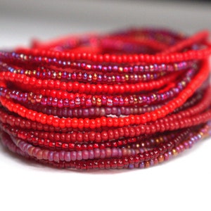 May include: A close-up of a stack of red and burgundy seed beads. The beads are arranged in a circular pattern, creating a layered effect.