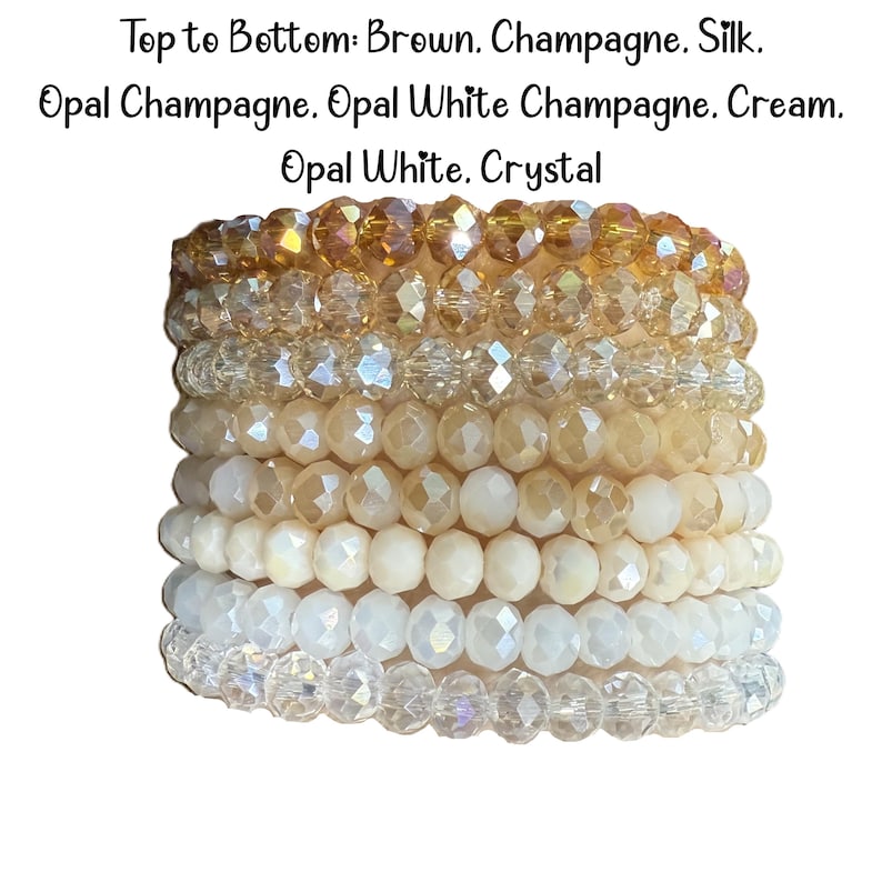 Peut inclure: Une pile de huit bracelets de perles avec des perles en cristal facett&eacute;es dans un d&eacute;grad&eacute; de couleurs. Le texte indique : Top to Bottom: Brown. Champagne. Silk. Opal Champagne. Opal White Champagne. Cream. Opal White. Crystal. Chaque bracelet est compos&eacute; de perles rondes et r&eacute;fl&eacute;chissantes.