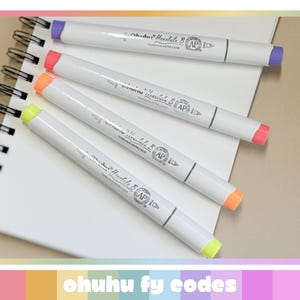 May include: Four white Ohuhu markers with coloured tips (purple, pink, orange, and yellow) are arranged diagonally on a white spiral notebook. The markers have text printed on them. The notebook is on a light beige surface. The text "ohuhu fy codes" is at the bottom.