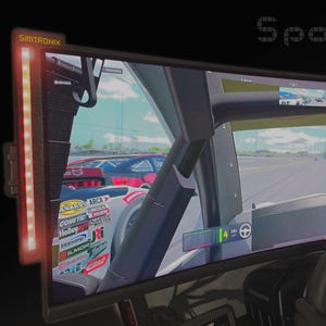 May include: A curved monitor showing a racing game, with the text "Spotter Mode" at the top. The steering wheel and dashboard are visible, along with a red light strip on the left. The game depicts race cars on a track.