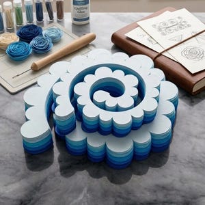 May include: A quilling art project in progress, featuring a large, layered paper flower in shades of blue and white. The image includes quilling supplies like glue, paper strips, and tools, with the text "The Quilling Collection" visible.