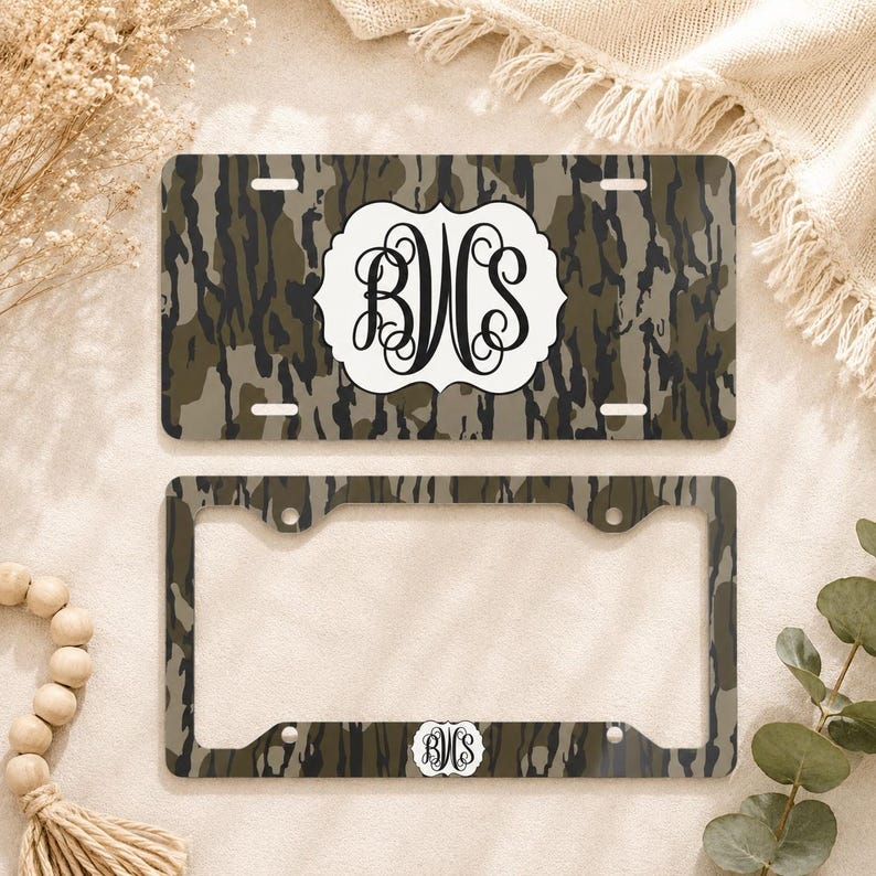 Op de afbeelding: Een kentekenplaat en frame set met een camouflagepatroon in groen, bruin en grijs. De kentekenplaat heeft een wit embleem met de zwarte initialen "BWS". Het frame heeft een bijpassend camouflagepatroon en een kleiner embleem.