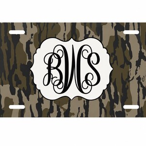 Op de afbeelding: Rechthoekige nummerplaat met een camouflagepatroon in bruin, groen en zwart. Een wit, sierlijk, ovaal embleem in het midden toont het monogram "BWS" in zwart schrift.