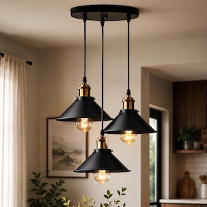 May include: A three-light pendant fixture featuring matte black conical metal shades with brass-toned accents. The lights are suspended from a circular black ceiling canopy by black cords, each housing a visible glowing Edison-style light bulb.