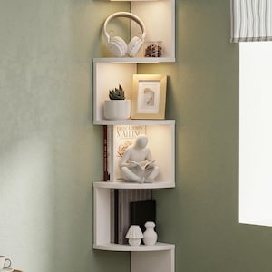 Peut inclure: Une étagère d'angle blanche avec éclairage intégré présente divers objets. Une plante en pot, un casque, un cadre photo, des livres et des objets décoratifs sont disposés sur les étagères. Les étagères sont fixées sur un mur vert.