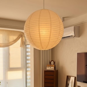 May include: A large, spherical paper lantern suspended from the ceiling. The lantern is a warm, off-white colour with vertical lines. The light from within illuminates the room. The lantern is a decorative lighting fixture.