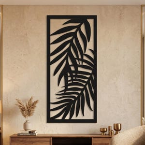 Peut inclure: Un panneau mural rectangulaire noir présentant un motif découpé au laser de deux feuilles de palmier superposées. La pièce est encadrée par une bordure noire solide et affiche un motif botanique détaillé sur toute la structure verticale.