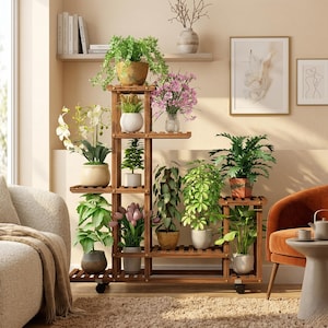 Peut inclure: Un présentoir à plantes en bois à plusieurs niveaux, orné de diverses plantes et fleurs en pot. Le présentoir est de couleur marron chaud et présente un design à lattes sur les étagères. Il est monté sur des roues. Les plantes comprennent du feuillage vert et des fleurs colorées.