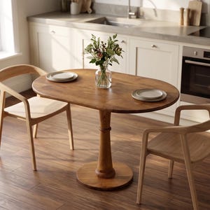 Può includere: Un tavolo da pranzo ovale in legno con due sedie abbinate. Il tavolo ha una base a piedistallo singolo ed è sormontato da due piatti. Un vaso di fiori è al centro. Le sedie sono in legno chiaro.
