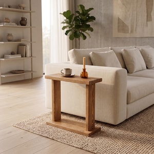 May include: A small, rectangular wooden side table with a natural finish. A cup and saucer, and a small brown bottle with a candle are on the table. The table sits on a woven rug in a living room setting.