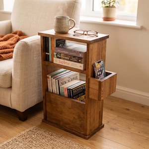 May include: A wooden side table with shelves and a phone holder. The table is filled with books and has a mug and glasses on top. The table is made of wood and has a warm, brown finish. The table is approximately 76 cm tall.
