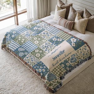 May include: A woven throw blanket featuring a patchwork design of blue and green floral patterns, gingham checks, and striped squares. The blanket includes a cream-colored section with the text "mom Jennifer heart of our home" in blue.