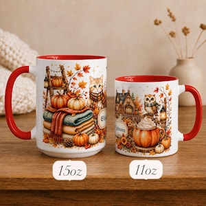 May include: Two white ceramic mugs with red interiors and handles. The 15oz mug features a cat, pumpkins, and folded blankets. The 11oz mug displays an owl, a house, and a pumpkin with whipped cream. Both mugs have autumn-themed illustrations.