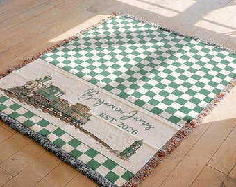 May include: A woven throw blanket featuring a green and white checkered pattern. One end displays a vintage-style green steam train illustration, a small lighthouse, and the personalized text Benjamin James EST. 2026 with fringed edges on all sides.
