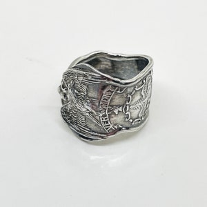 May include: Silver ring made from a repurposed coin featuring an eagle and the words "E Pluribus Unum".