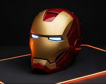 May include: A red and gold Iron Man helmet with glowing blue eyes. The helmet is on a dark surface with an orange glowing outline. The helmet is a replica of the one worn by the Marvel Comics superhero.