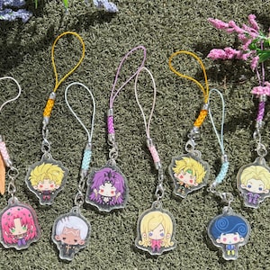 Puede incluir: Una colección de ocho dijes de acrílico con personajes de anime estilo chibi con colores de cabello y atuendos distintos. Cada dije está sujeto a un lazo de cordón trenzado de colores con un cierre de metal plateado, mostrando varios diseños.