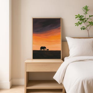 May include: Framed art print featuring a sunset scene with two elephant silhouettes. The sky transitions from dark purple to vibrant orange and yellow. The artwork is displayed on a wooden nightstand next to a bed with white bedding.