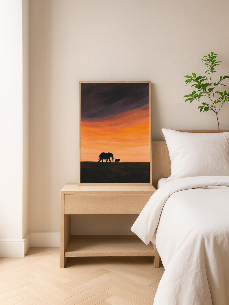 May include: Framed art print featuring a sunset scene with two elephant silhouettes. The sky transitions from dark purple to vibrant orange and yellow. The artwork is displayed on a wooden nightstand next to a bed with white bedding.