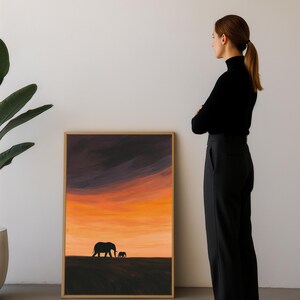 May include: Framed art print featuring a silhouette of two elephants against a vibrant sunset sky. The artwork showcases a warm palette of orange, yellow, and purple hues, with a simple, elegant design. The frame is a natural wood color.