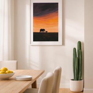 May include: Framed art print featuring a silhouette of two elephants against a vibrant sunset sky. The artwork showcases a warm palette of orange, yellow, and purple hues, creating a serene and natural scene. The print is displayed in a white frame.