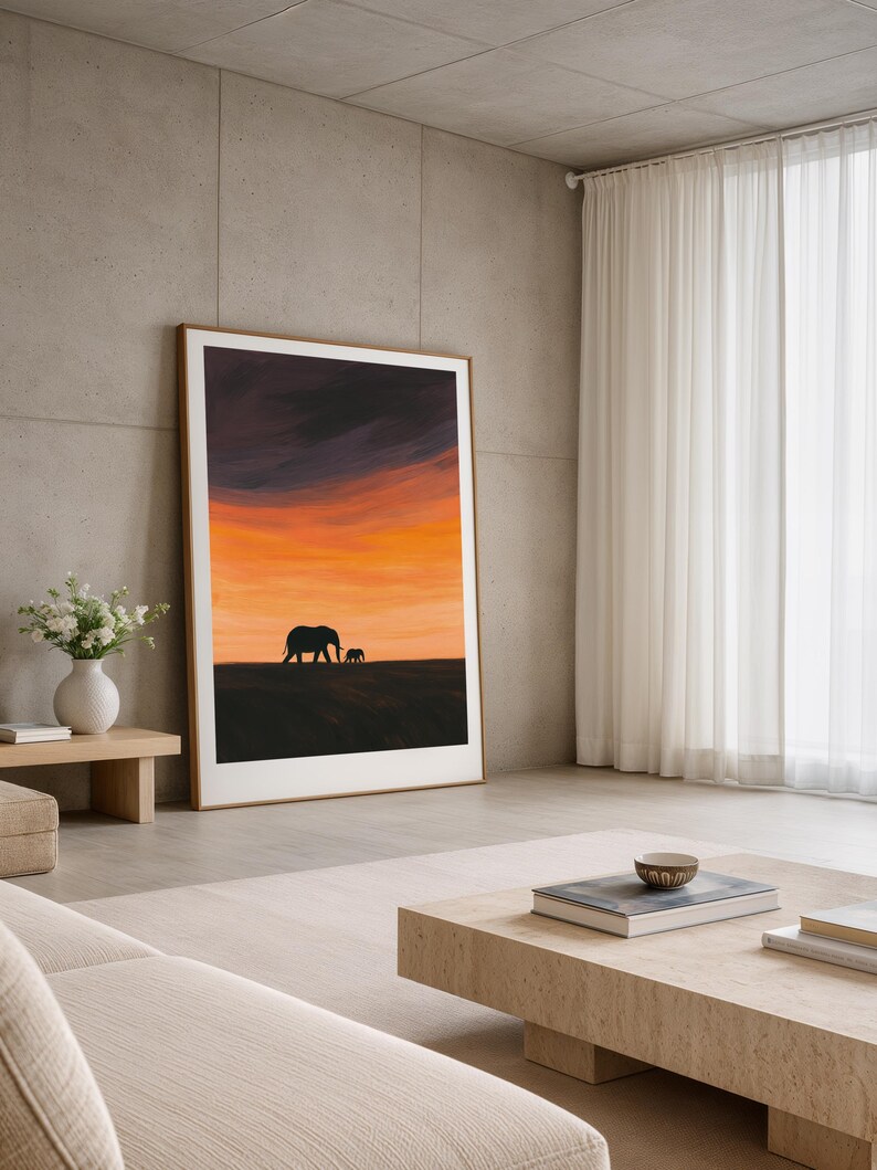 May include: A framed art print featuring a silhouette of two elephants against a vibrant sunset sky. The artwork has a warm color palette of orange, yellow, and purple. The print is displayed in a modern living room setting with neutral tones.