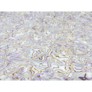 Pode incluir: Close-up de uma superfície com um padrão em espiral. O design apresenta uma mistura de tons brancos, roxos claros e castanhos, criando um efeito marmorizado. A textura parece lisa e refletora, com um brilho subtil.