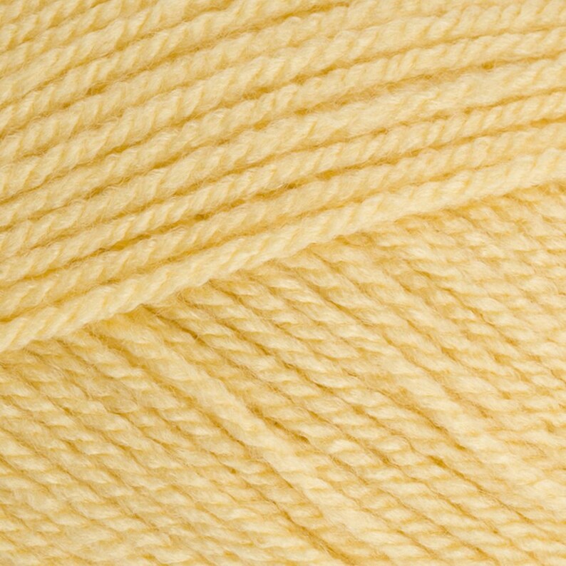 May include: Close-up of a skein of soft, pale yellow yarn. The yarn is tightly wound, showing individual strands and a textured surface. The colour is a warm, creamy yellow, ideal for knitting or crocheting projects.