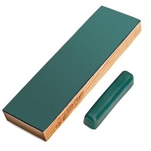 May include: A green sharpening strop with a wooden base and a small green sharpening compound stick. The strop has the words "Beaver Craft" printed on the side. The wooden base is made of light-coloured wood.
