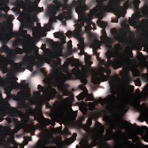 May include: A close-up of a surface with a tortoiseshell pattern. The pattern features irregular shapes in shades of black and brown, interspersed with lighter, almost white, areas. The overall effect is a mottled, textured appearance.