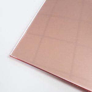 May include: A close-up of a sheet of rose gold mirror acrylic. The acrylic is smooth and reflective, with a slight sheen.