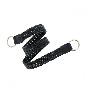 Puede incluir: Cinturón de cuero trenzado negro con anillos de metal plateado. El cinturón presenta un diseño tejido y es adecuado para varios atuendos. Un accesorio versátil para el uso diario.