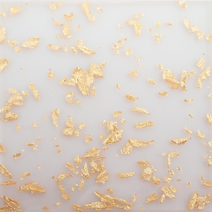 May include: White background with gold flakes scattered across the surface.