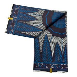 May include: Folded fabric with a dark blue background and a repeating pattern of blue and white leaf-like shapes. The fabric has a border with floral designs and the text "GUARANTEED R".