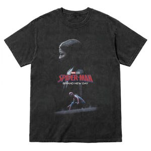 May include: Dark gray t-shirt featuring a graphic from the Marvel Studios Spider-Man movie. The design includes a silhouette of a person, the Spider-Man logo, and the text "Brand New Day".