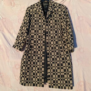 May include: A long, open-front coat with a black and tan checkered pattern. The coat has a notched collar and three-quarter sleeves. The coat is hanging on a black hanger.