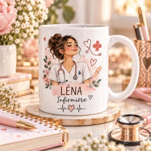 Pode incluir: Uma caneca de cerâmica branca com uma ilustração gráfica de um enfermeiro com estetoscópio, rodeada por detalhes florais cor-de-rosa, corações, uma cruz médica e um penso. O texto diz LÉNA e Infirmière, com uma linha de batimento cardíaco.
