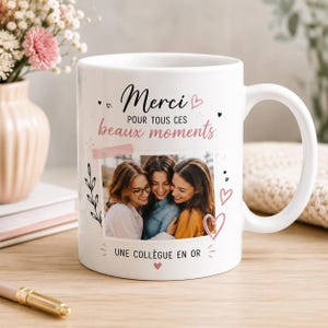 Peut inclure: Un mug en céramique blanc orné d'une photographie de trois personnes, avec le texte "Merci POUR TOUS CES beaux moments" et "UNE COLLÈGUE EN OR" imprimé en noir et rose, agrémenté de petites illustrations de cœurs et de feuilles.