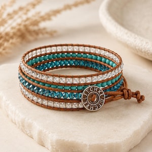 May include: Wrap bracelet with turquoise and clear crystal beads, and brown leather. The bracelet has multiple strands of beads and leather, and a button clasp. The bracelet is approximately 19 cm long.