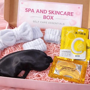 Puede incluir: Una caja rosa con la etiqueta "SPA AND SKINCARE BOX" llena de artículos de cuidado personal. Incluye una máscara para los ojos negra, diademas blancas y mascarillas para los ojos de vitamina C amarillas. La caja está forrada con papel rosa.