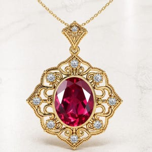 May include: A gold pendant necklace featuring a large, oval-cut deep red gemstone at the center. The gold setting is ornate with intricate scrollwork and is accented by eight small, round, clear white diamonds set around the central stone.