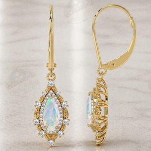 May include: A pair of gold leverback earrings featuring a central pear-shaped iridescent opal gemstone surrounded by a halo of small round white diamonds. The metal setting has a textured, intricate design around the pear-shaped center stone.