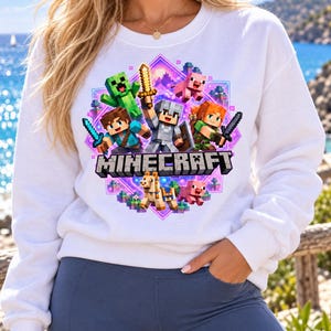 May include: A white long-sleeve sweatshirt featuring a colorful graphic print of Minecraft characters including a Creeper, Steve, Alex, a pig, and a llama. The design is set against a purple diamond background with the Minecraft logo text below.